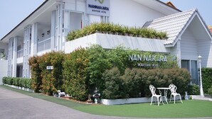 A hotel with a white facade, a sign reading "Nannakara Boutique Hotel," and outdoor seating with chairs. - Nan Nakara Boutique (Nan)