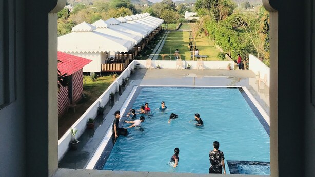 A pool area with people swimming, surrounded by a garden and a view of distant hills. - Hotel Green Haveli (Pushkar)