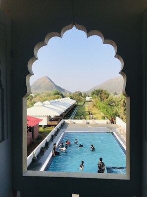 A pool area with people swimming, surrounded by a garden and a view of distant hills. - Hotel Green Haveli (Pushkar)
