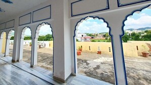 A corridor with arches leading to a courtyard with potted plants and buildings in the background. - Hotel Green Haveli (Pushkar)