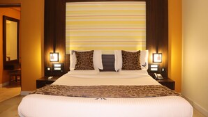 Habitación de hotel con una cama grande, dos mesitas de noche con lámparas, un espejo y una ventana con cortinas a rayas.