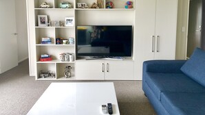 A living room with a white entertainment unit, a flat-screen TV, a blue sofa, and a coffee table. - Lovely Sunny Home Sweet Home (Christchurch)