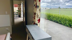 A room with a view of a green hedge and a white fence. There is a bed with a white headboard and a bedside table. - Lovely Sunny Home Sweet Home (Christchurch)