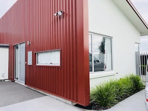 Ein modernes Gebäude mit roter Fassade, einem weißen Fenster und einer kleinen Grünfläche.