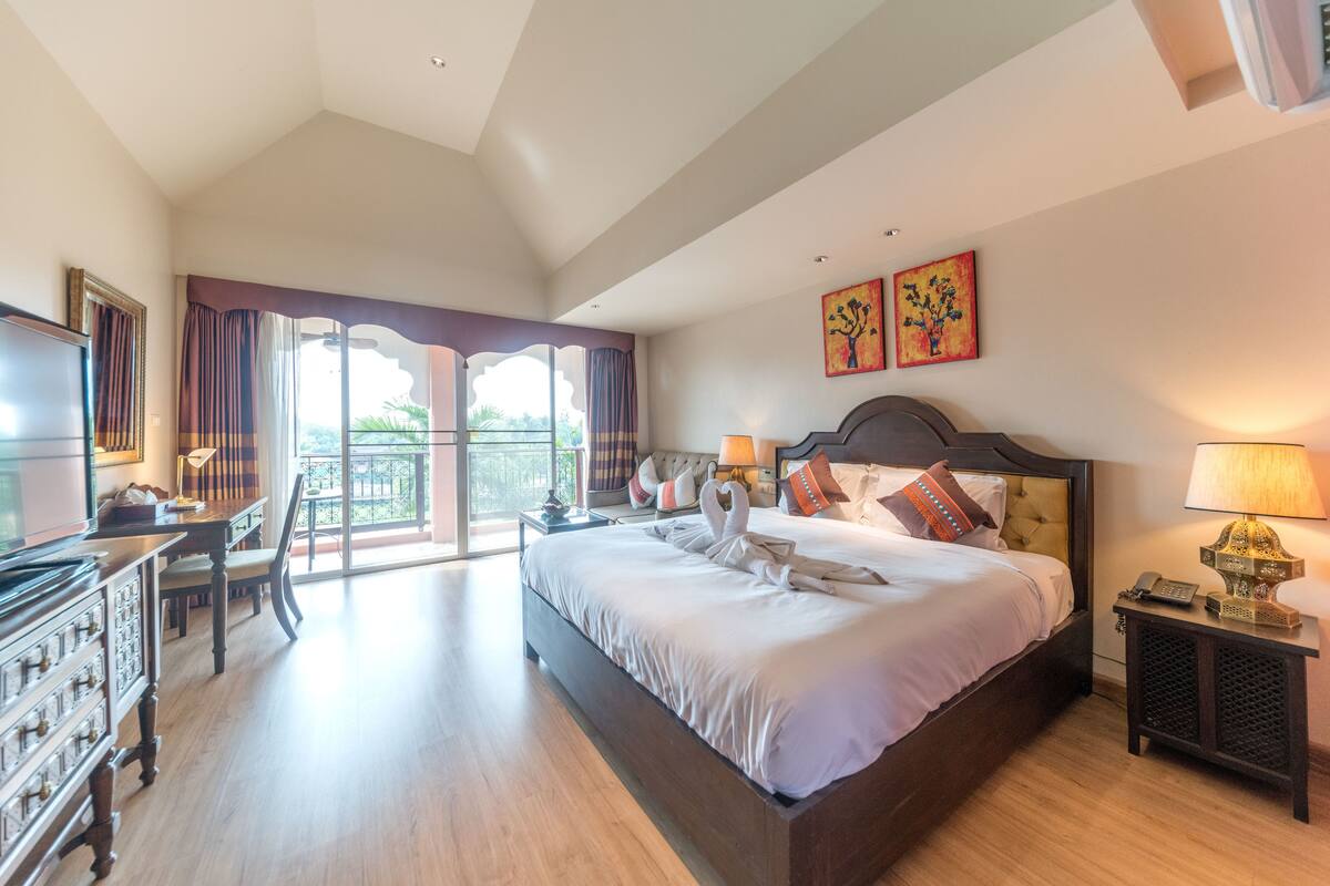 A spacious bedroom with a large bed, a desk, and a television.