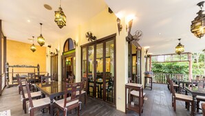 A spacious outdoor dining area with wooden tables and chairs, hanging lanterns, and a view of greenery. - Sheik Istana Hotel Chiangmai  (Chiang Mai)
