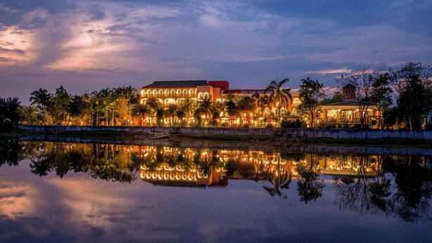 A waterfront hotel with a reflection in the water, featuring a large building with arched windows and a red roof, surrounded by palm trees. - Sheik Istana Hotel Chiangmai  (Chiang Mai)