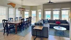 A spacious living area with a dining table, chairs, a sofa, a coffee table, and a ceiling fan. - Sea the Love | Oceanfront, Oceanside Hot Tub + Elevator (North Topsail Beach)