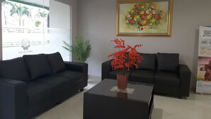 A reception area with two black sofas, a coffee table, a potted plant, and a framed floral painting on the wall. - Green Lake View Luxury Apartment by Indah (South Tangerang)