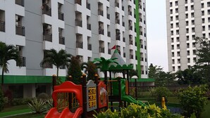 A playground with a red slide and a green climbing structure, surrounded by lush greenery. - Green Lake View Luxury Apartment by Indah (South Tangerang)