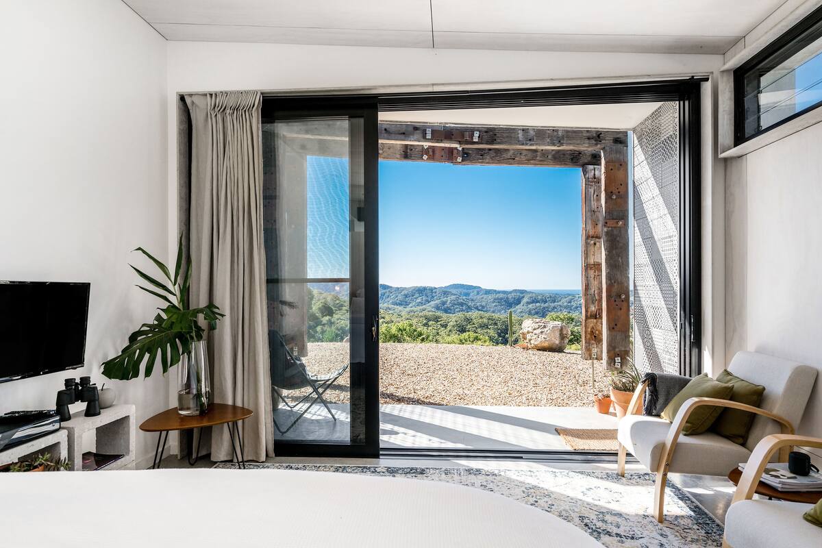 Une chambre moderne dotée d’une grande porte-fenêtre coulissante donnant sur une terrasse avec vue sur les montagnes.