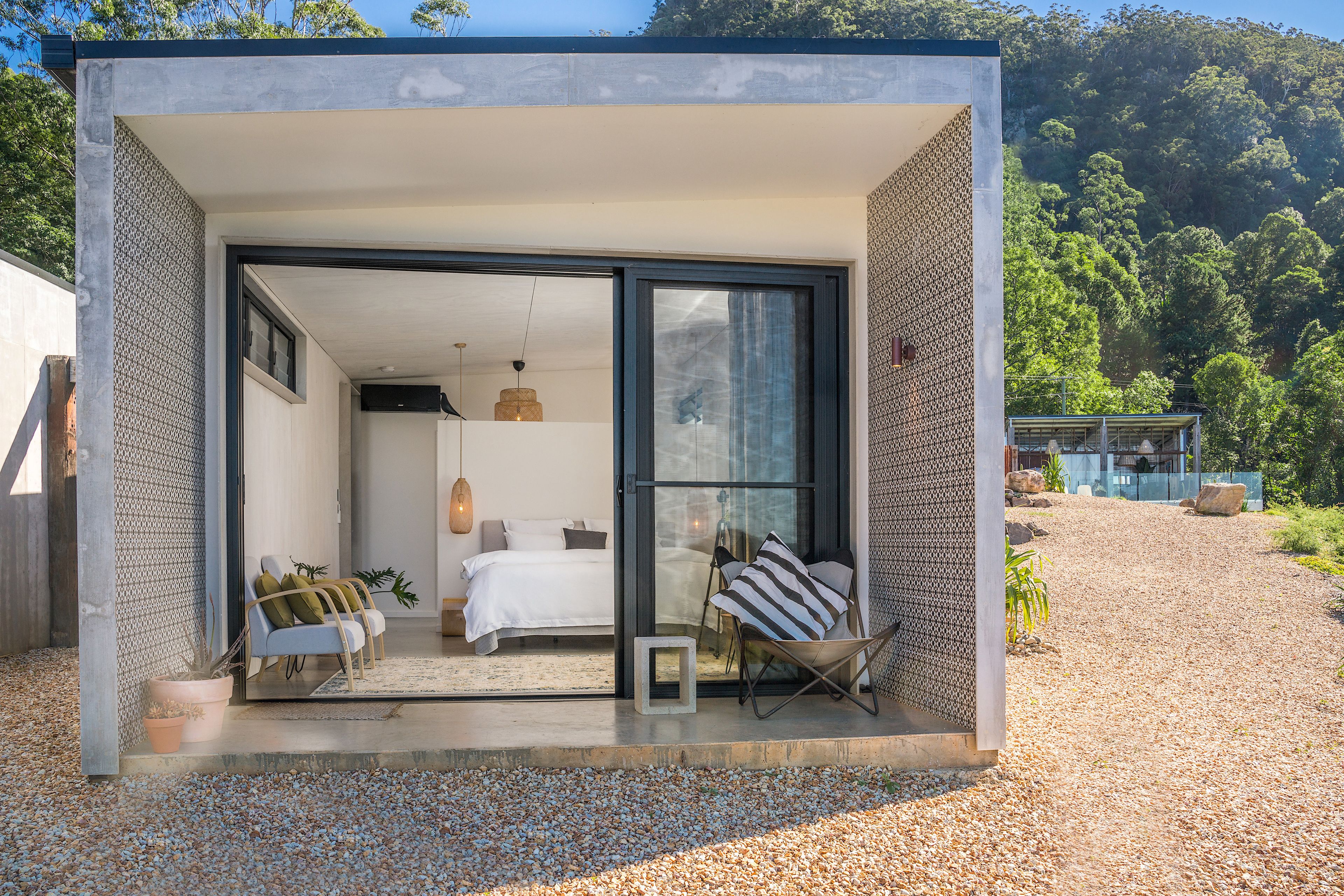 A modern, compact house with a bedroom featuring a bed, bedside tables, and a chair.