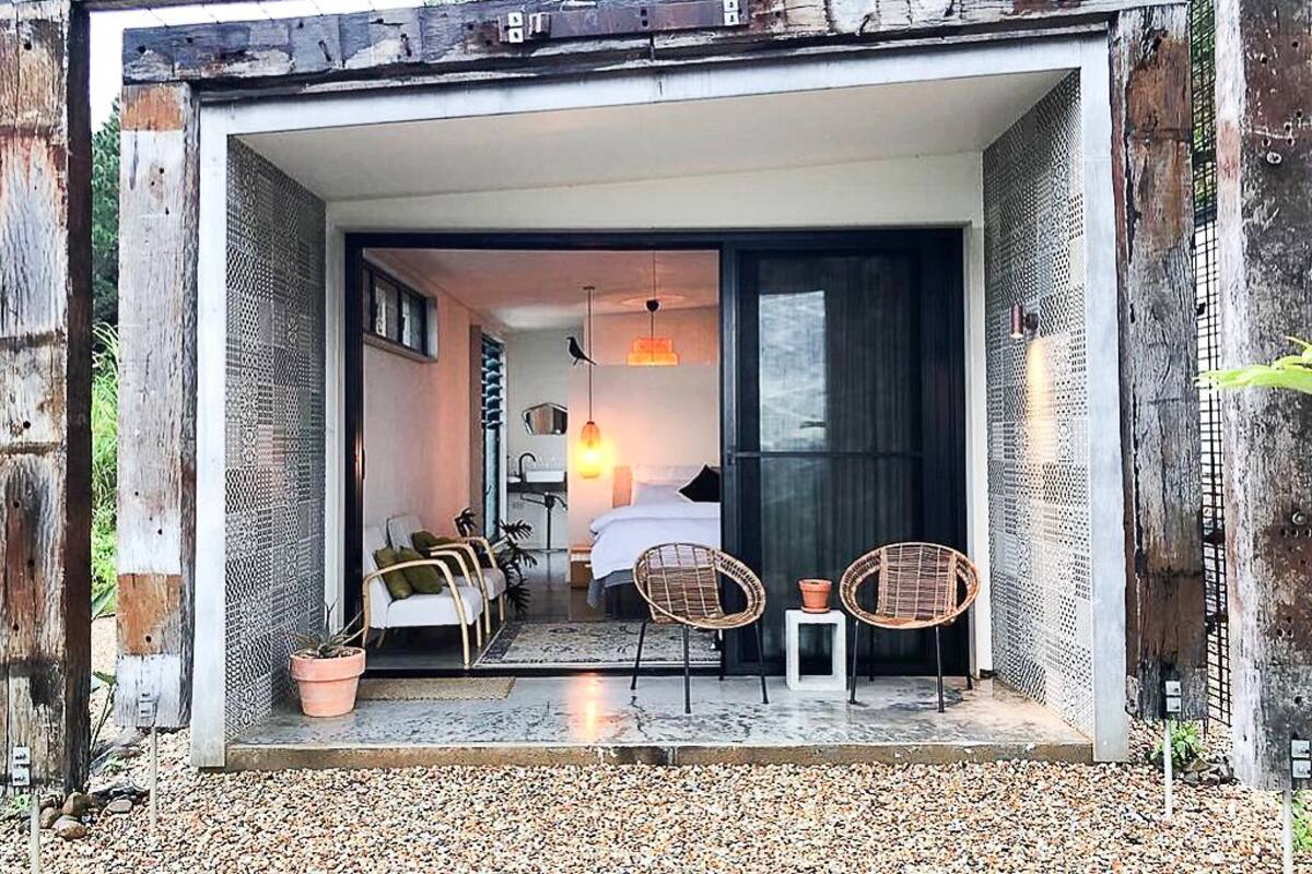 Un intérieur moderne comprenant un lit, deux fauteuils en osier, une petite table et un luminaire suspendu.