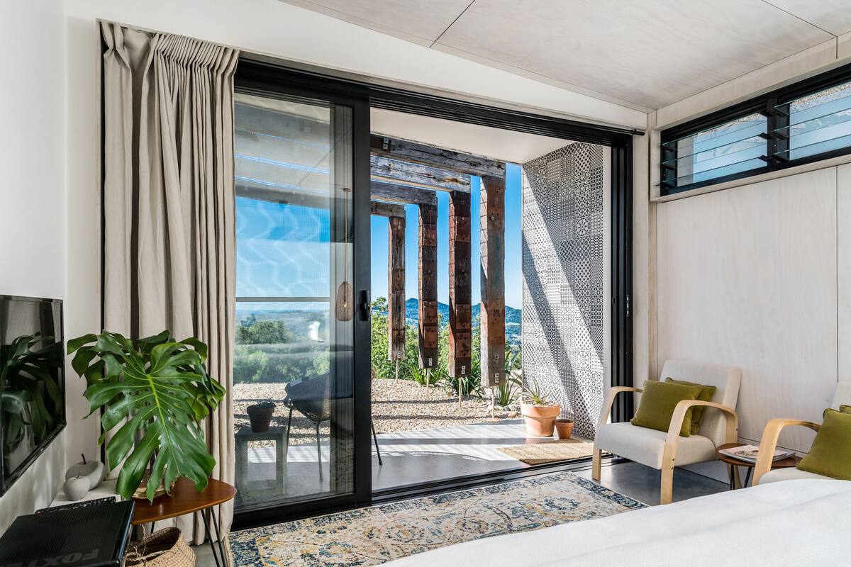 Une chambre d’hôtel moderne dotée d’une grande porte-fenêtre coulissante donnant sur un balcon, d’un lit, d’un bureau et d’une chaise.