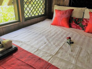 Een keurig opgemaakt bed met een witte dekbedovertrek, rode kussens en een enkele roos op het bed.