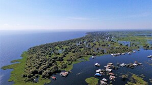 Vista aérea de una zona costera con numerosos barcos amarrados a la orilla, rodeada de vegetación densa y una vista despejada del mar.