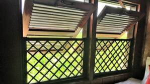 Una habitación con una cama, un ventanal de celosía y vistas a zonas verdes.