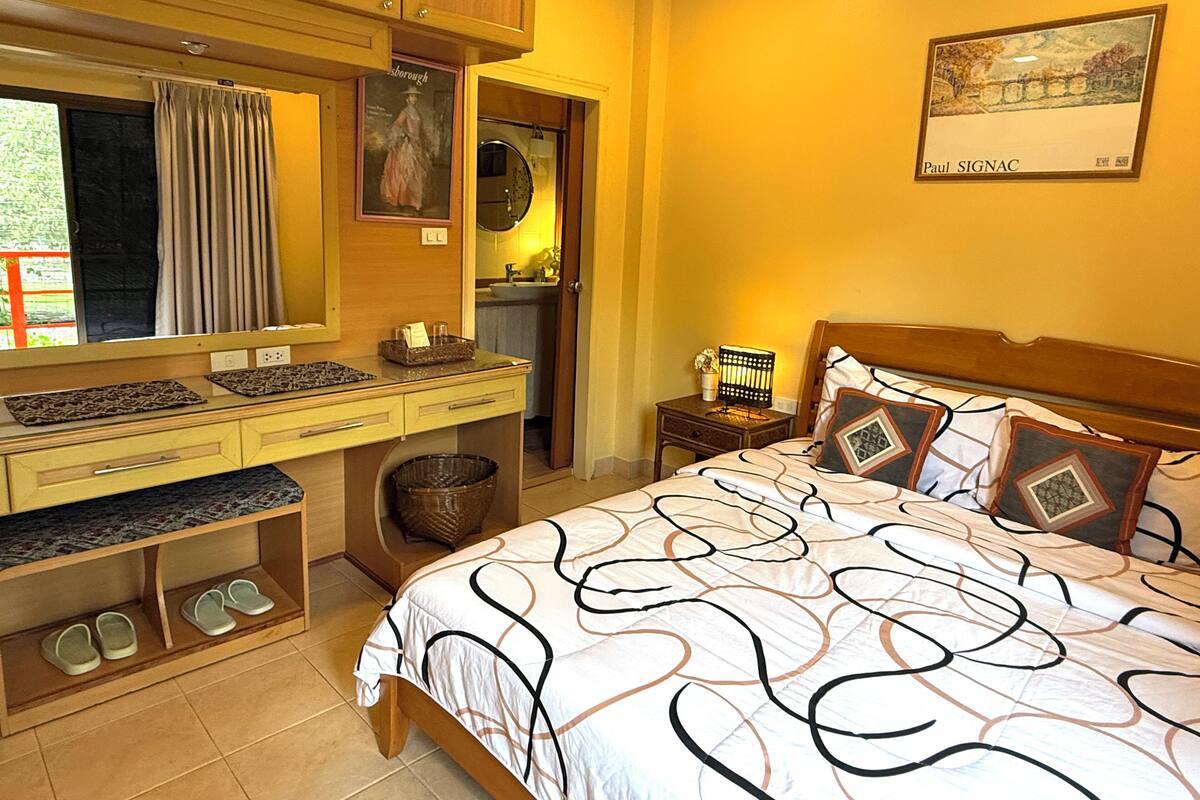 A bedroom with a bed, a desk, a mirror, and a nightstand.