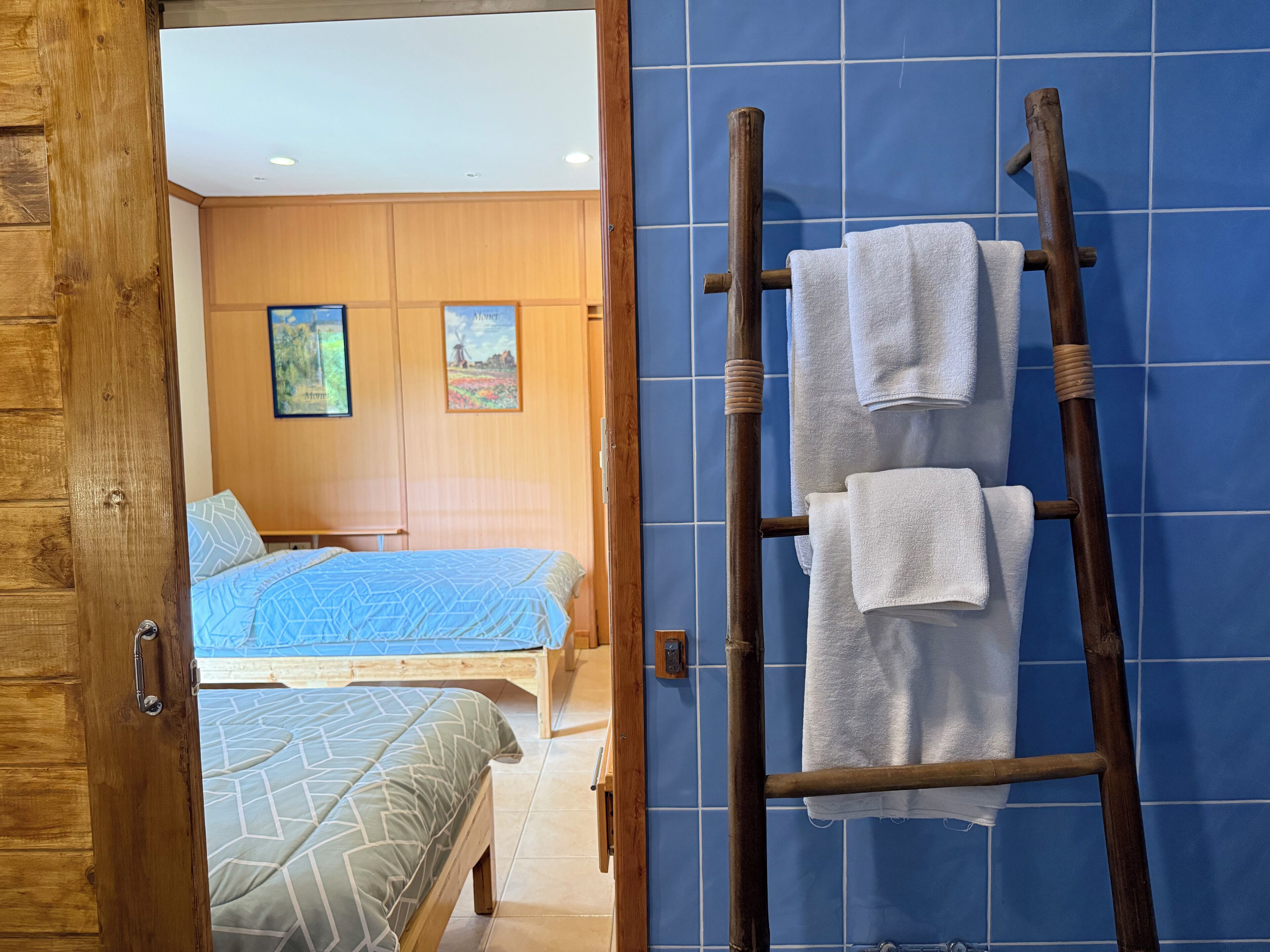A bedroom with a bed, a wooden ladder with towels, and a blue tiled wall.
