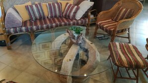 Uma sala de estar com mesa de centro de vidro, sofá com almofadas listradas e poltrona de vime.