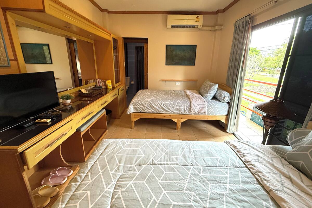 A bedroom with a bed, a TV, a dresser, and a window with a view.