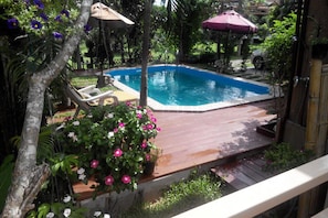 Ein Schwimmbecken mit Holzterrasse, umgeben von üppiger Vegetation und einigen Liegestühlen.