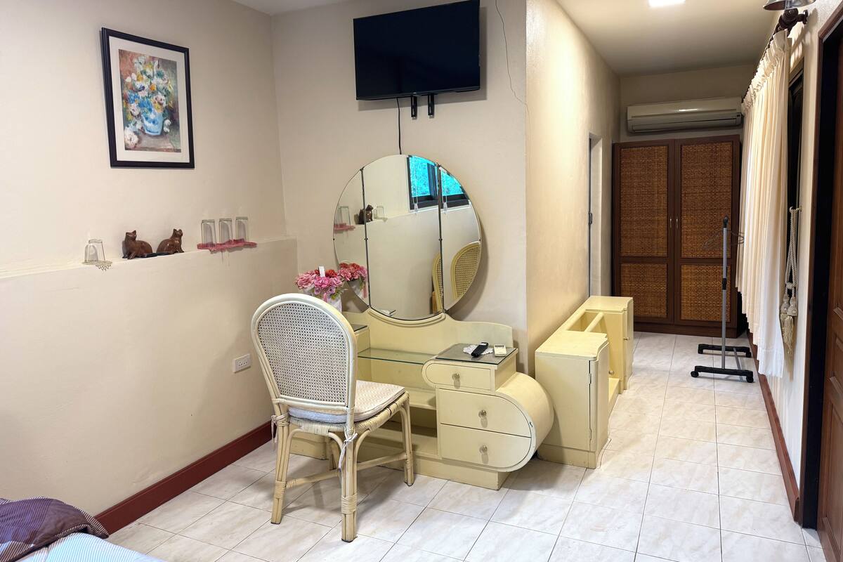 A hotel room with a bed, a chair, a vanity with a mirror, a television, and a wardrobe.