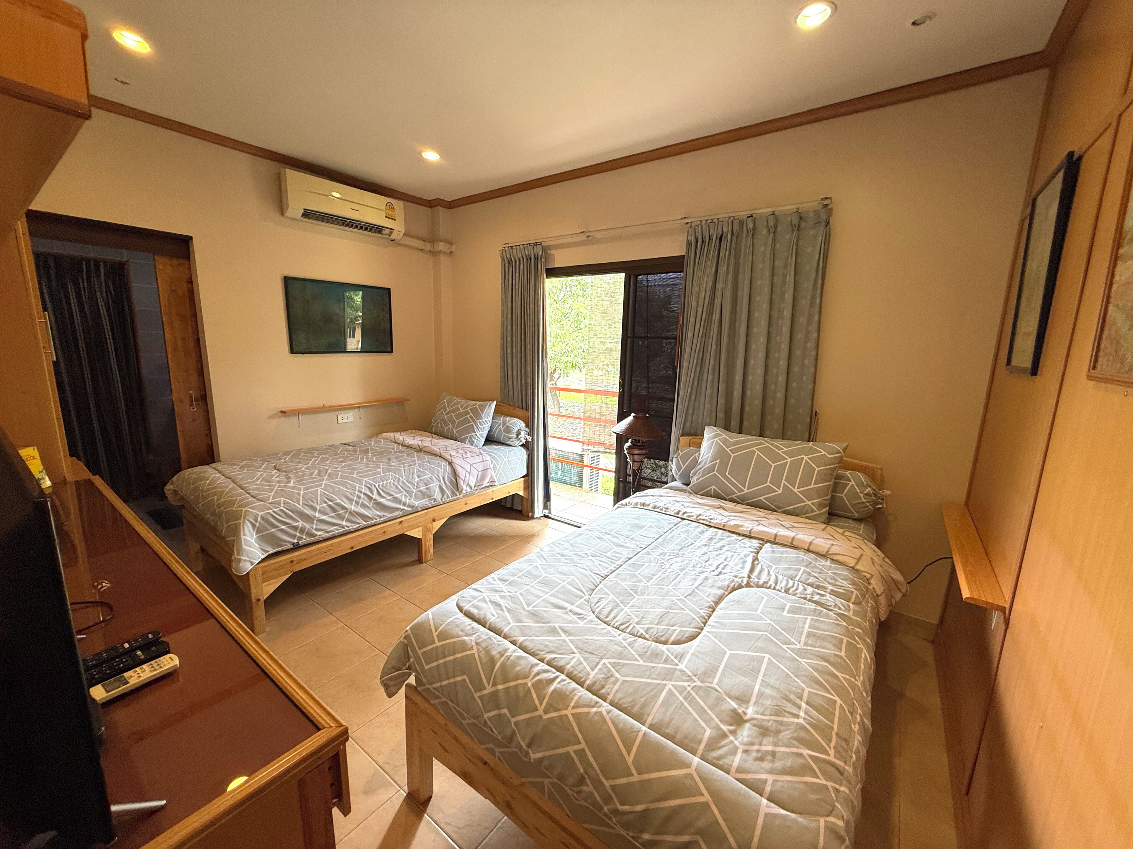 A bedroom with two single beds, a desk, and an air conditioning unit.