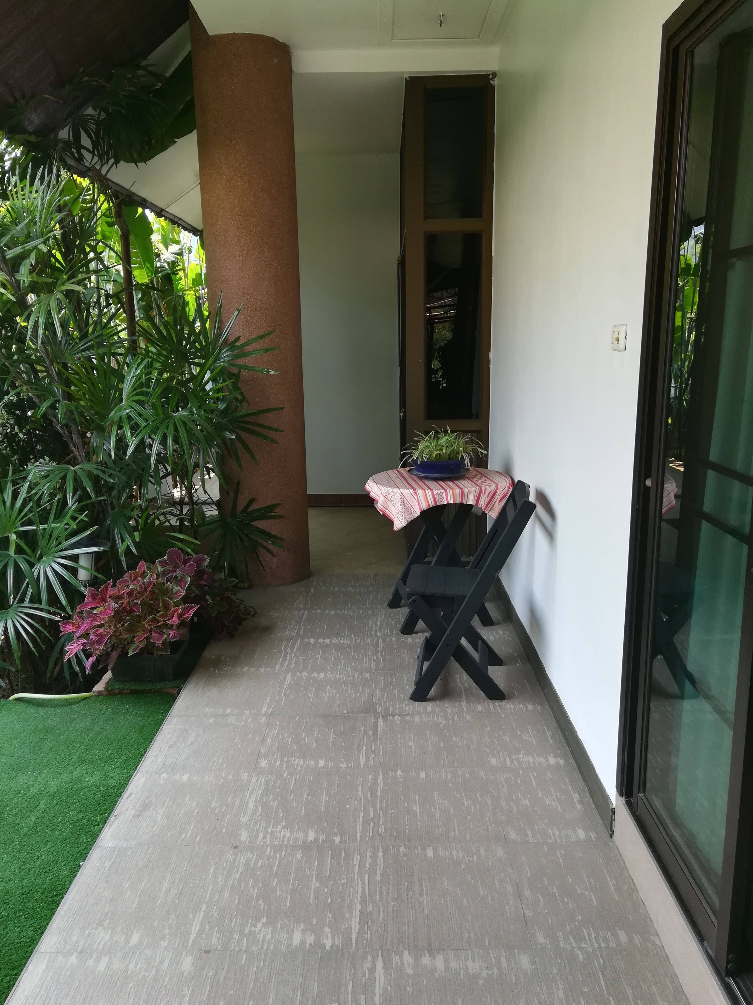 A covered outdoor area with a table and chairs, surrounded by potted plants and a green artificial turf.