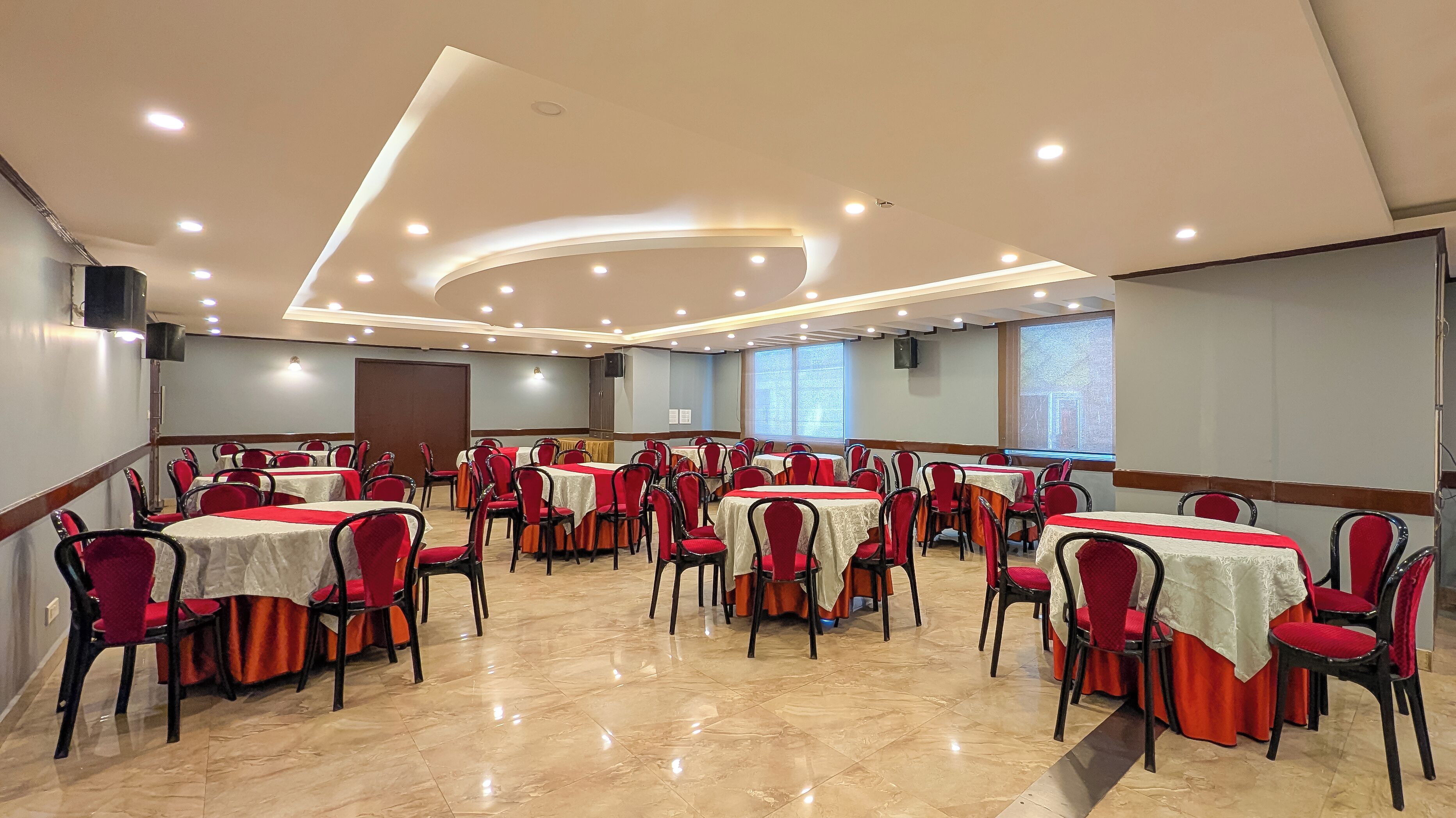 A conference room with multiple tables and chairs, equipped with ceiling lights and a projector screen.