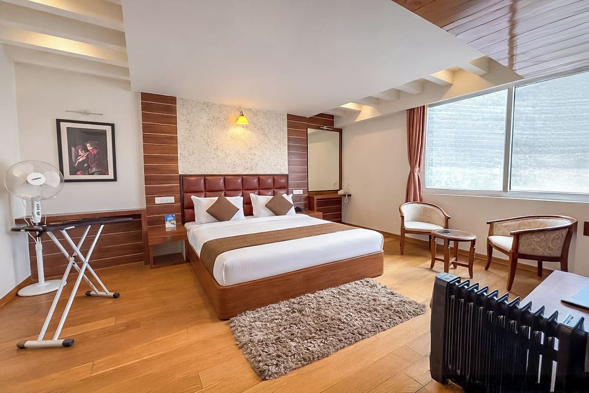 Una habitación de hotel moderna con una cama grande, un escritorio, una silla, un radiador y una ventana con vistas.