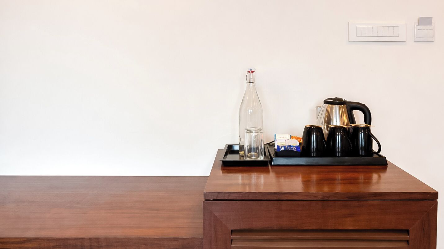 A wooden desk with a glass bottle, a glass, and a coffee maker.