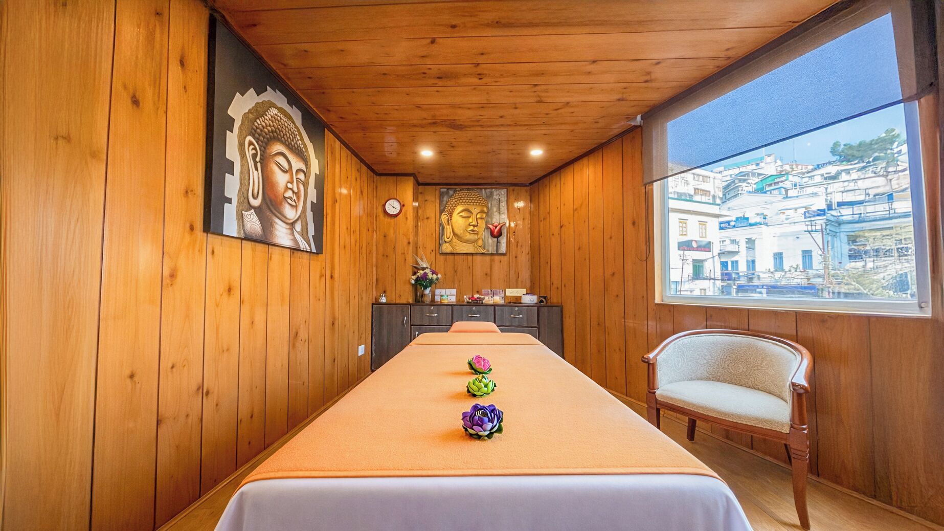 A room with wooden walls, a long table with a white tablecloth, a chair, and a Buddha statue on the wall.