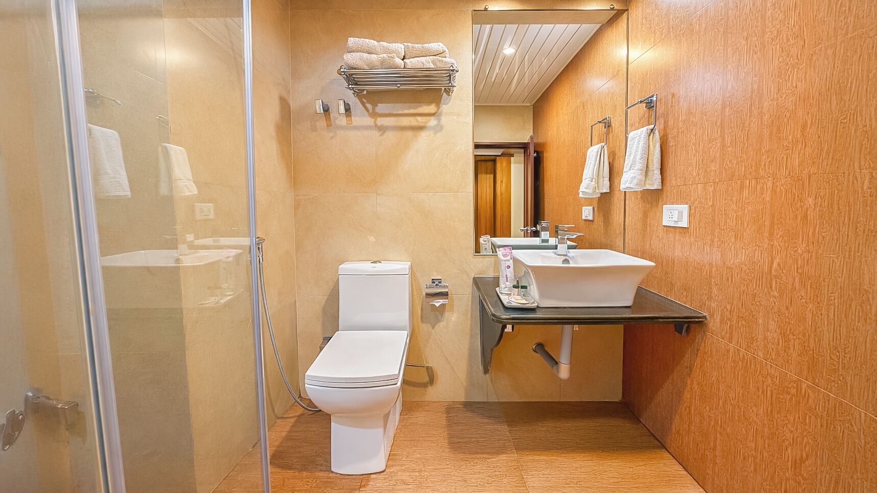 Un baño pequeño con cabina de ducha de vidrio, inodoro blanco, lavamanos con espejo y paredes de madera.