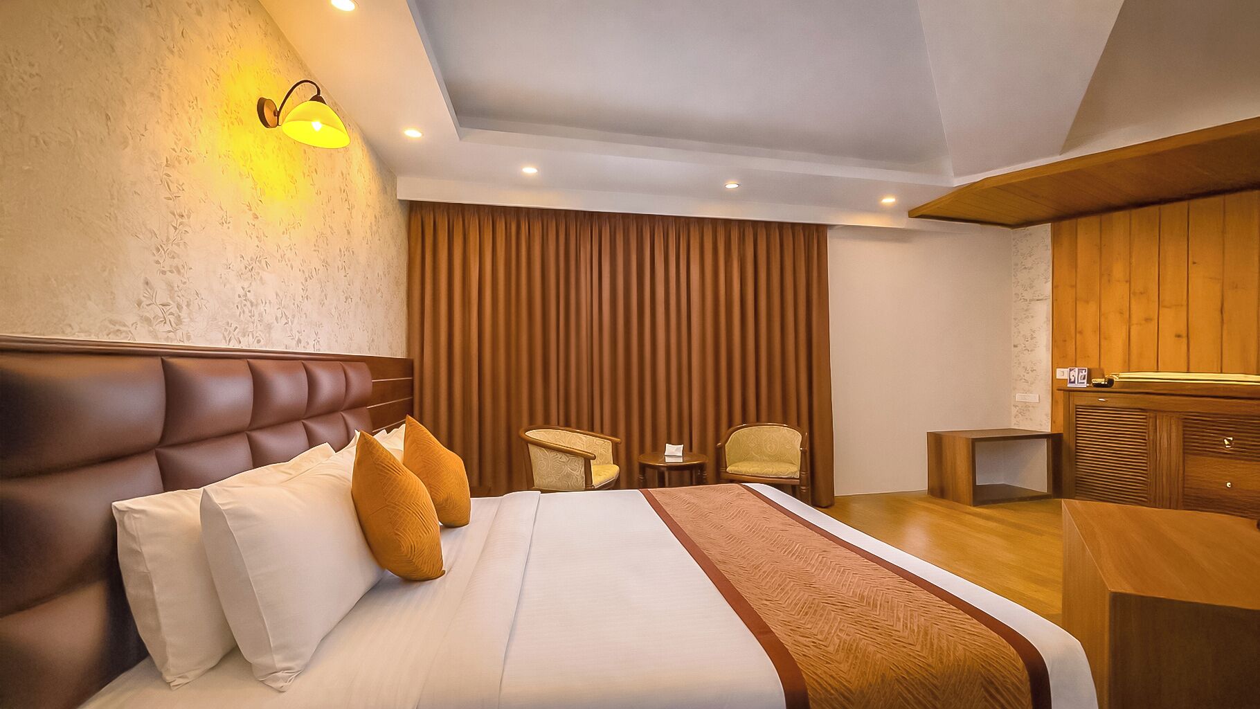 A hotel room with a large bed, two chairs, a small table, and a wooden desk.
