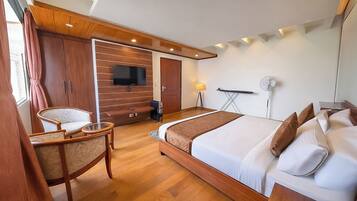 Una habitación de hotel moderna con una cama de madera, un televisor montado en la pared, un escritorio con una silla y un ventanal grande.