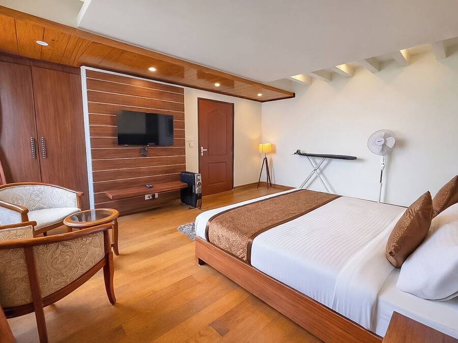 Una habitación de hotel moderna con una cama de madera, un televisor montado en la pared, un escritorio con una silla y un ventanal grande.