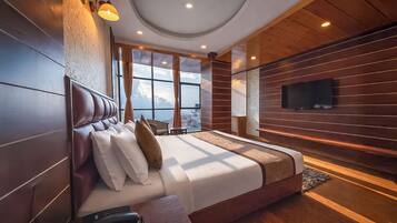 Quarto de hotel moderno com uma cama grande, televisão de tela plana na parede e vista para a cidade por grandes janelas.