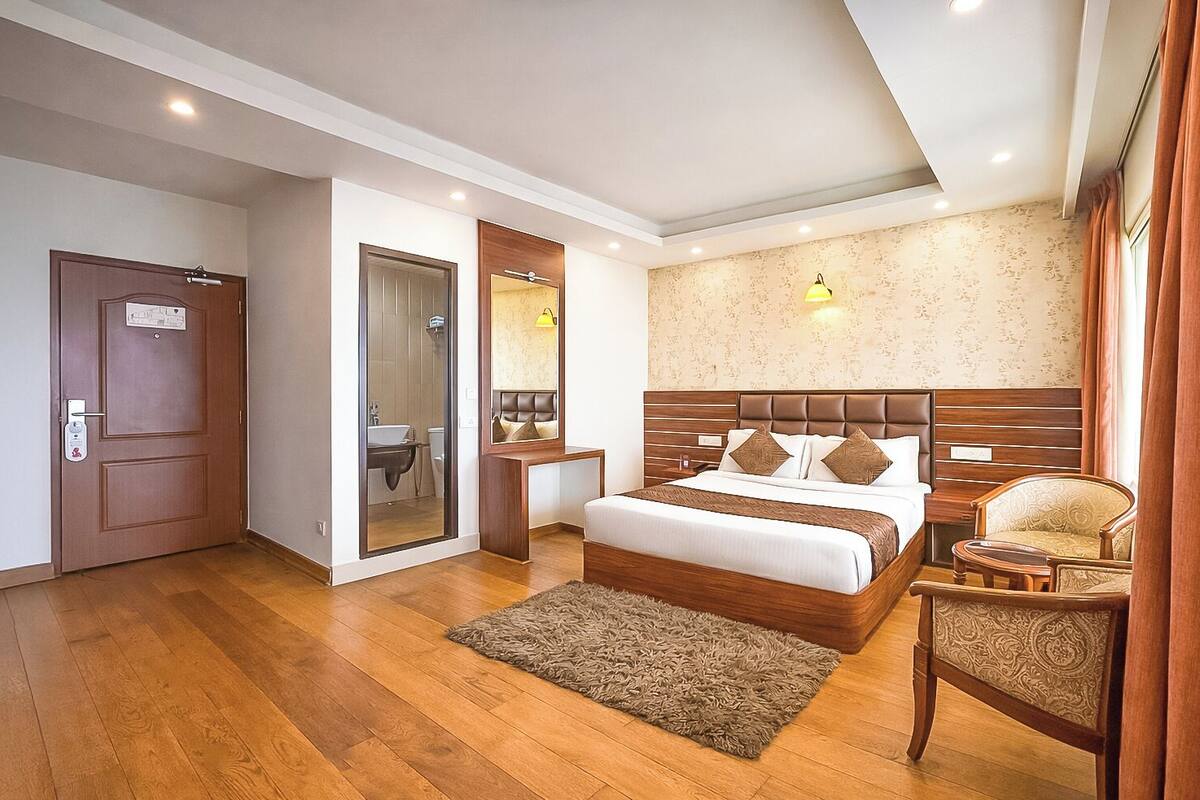 Una habitación de hotel con suelo de madera, una cama con cabecero, una mesita de noche, una silla y un espejo.