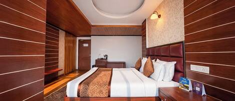 Une chambre d’hôtel avec un décor de panneaux en bois, un grand lit avec de nombreux oreillers, une table de chevet et un bureau avec une lampe.