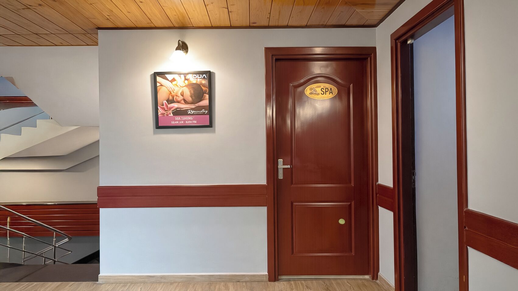 Rebedor d'hotel amb una porta de fusta amb la inscripció "SPA", un cartell publicitari d'un servei d'spa i una escala.