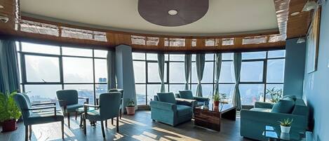 A spacious lounge with a high ceiling, large windows offering a city view, and comfortable seating areas.