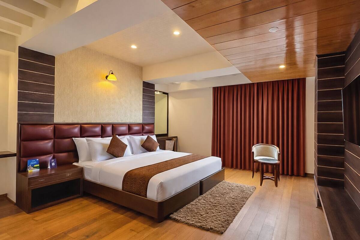 Habitación de hotel con una cama grande, cabecera de madera, televisor de pantalla plana en la pared, mesita de noche y una silla.