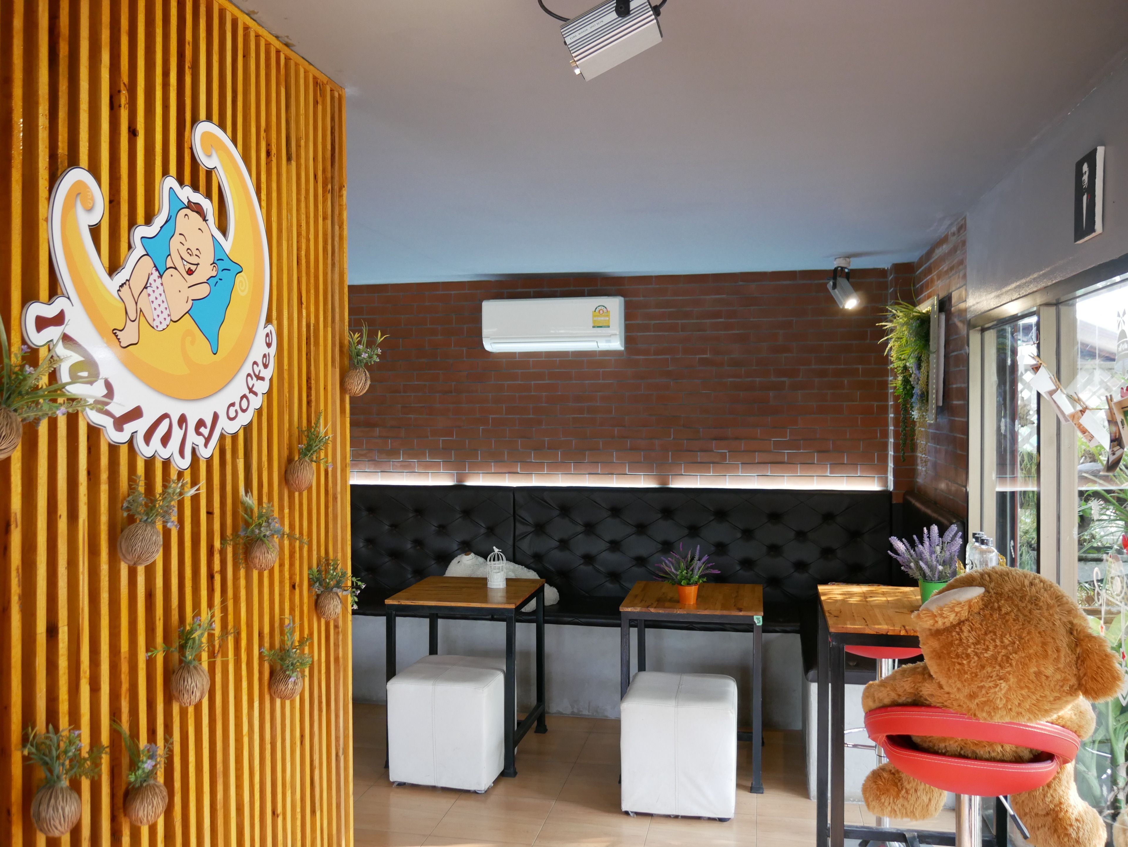 Een gezellig café interieur met een houten accentmuur, een zwarte met kussens beklede bank en een teddybeer decoratie.