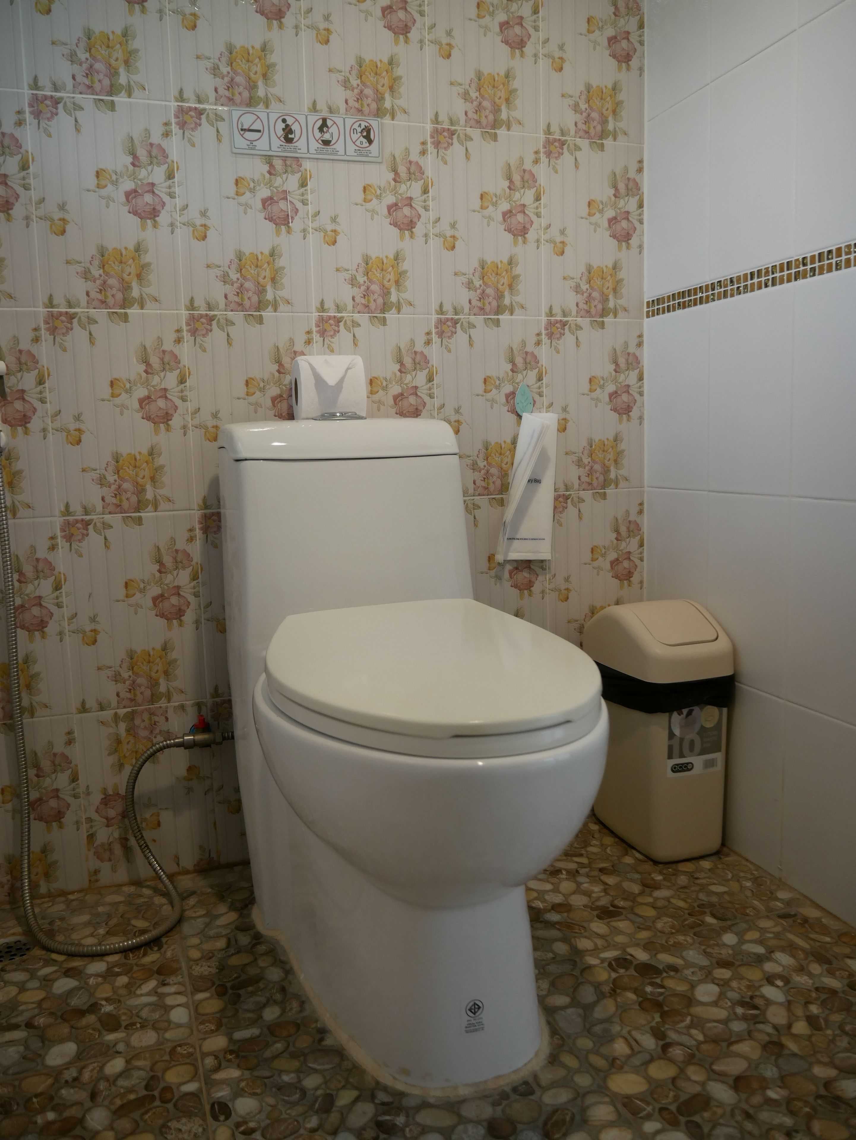 A bathroom with a toilet, a trash bin, and a shower.