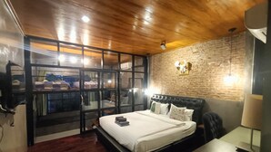 Ein modernes Schlafzimmer mit Holzboden, einer Ziegelwand, einem großen Bett mit weißer Bettwäsche und Blick durch eine Glasabtrennung.