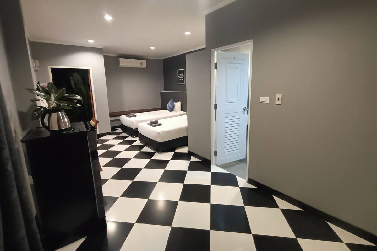 Una habitación de hotel con piso a cuadros, dos camas, una planta y una cafetera.