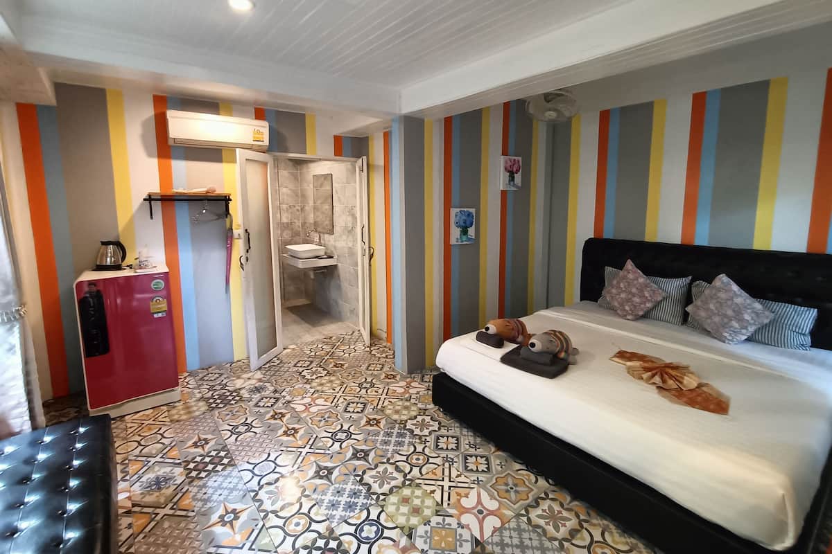 Un dormitorio con suelo estampado, una cama con almohadas, una mesita de noche, un armario rojo y un baño con ducha y lavabo.