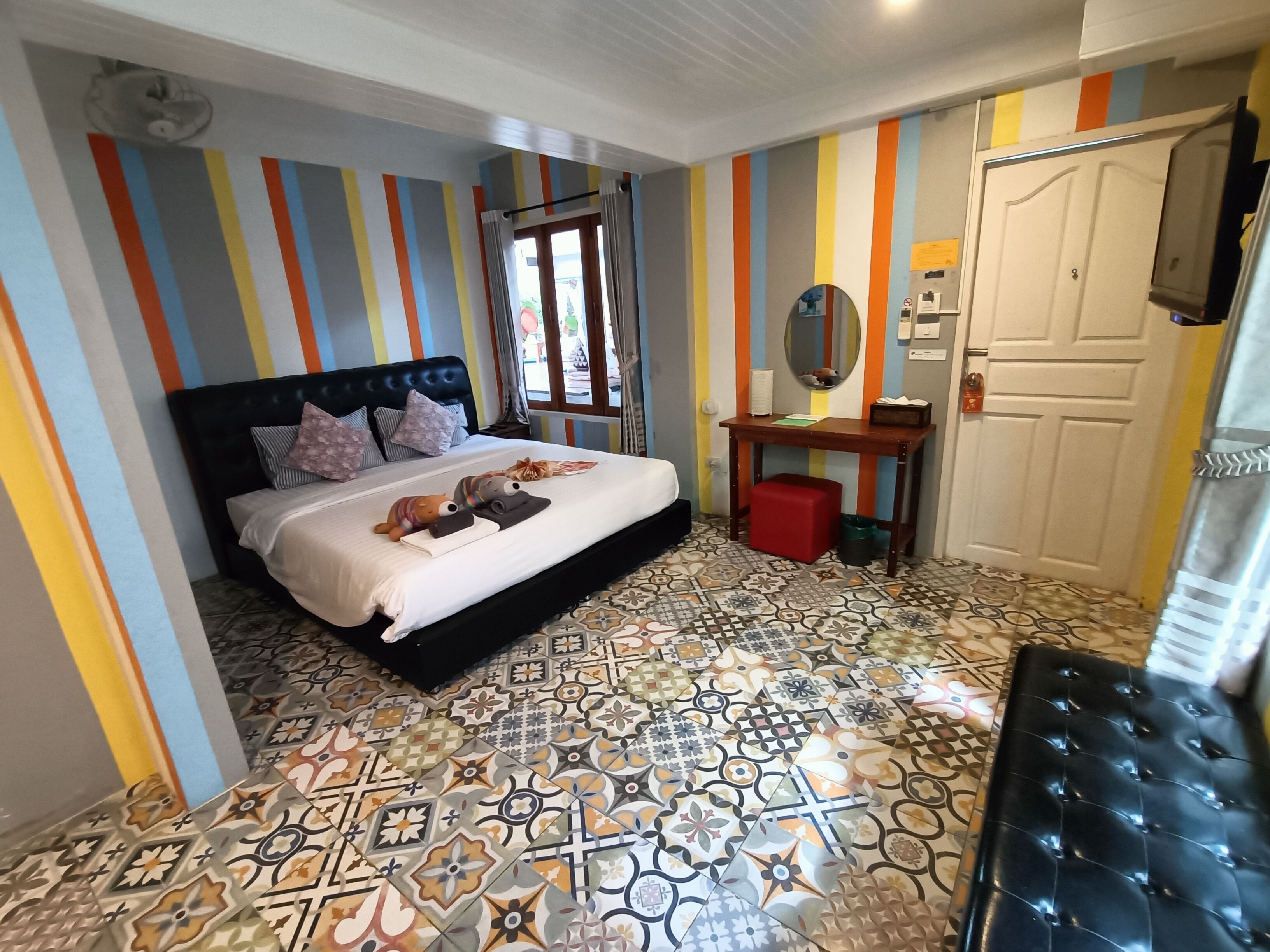 Une chambre avec des murs à rayures, un lit avec des oreillers, une table de chevet avec un miroir et des carreaux de sol à motifs.