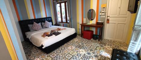 Une chambre avec des murs à rayures, un lit avec des oreillers, une table de chevet avec un miroir et des carreaux de sol à motifs.